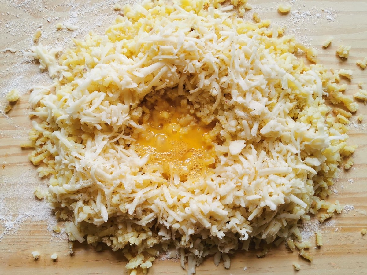 Riced potato and grated cheese on wood surface with beaten egg in the centre.