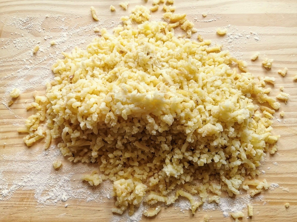 Pile of riced cooked potato on wood surface dusted with flour.