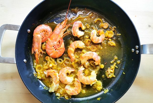 unpeeled prawns and peeled prawns in skillet with cooked onions and prawn saffron broth