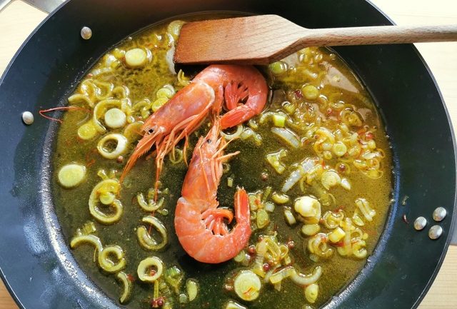 2 unpeeled prawns in skillet with cooked onions and prawn saffron broth