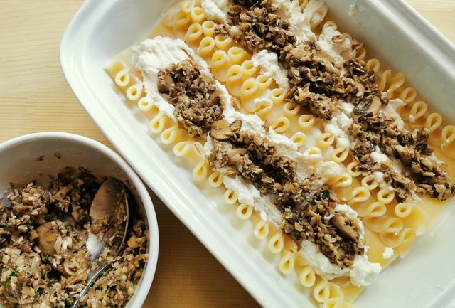 2 lasagne covered with chopped mushrooms and ricotta in white rectangular oven dish.