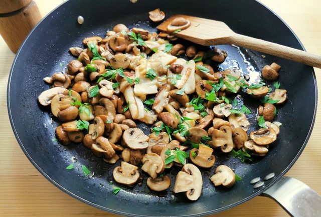 cremini and porcini mushrooms cooking in skillet with parsley and garlic