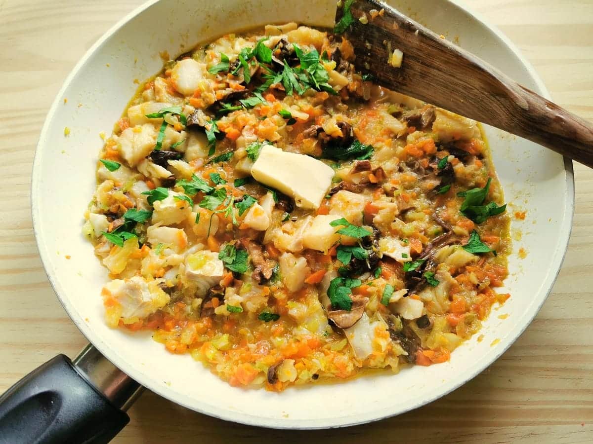 Fresh parlsley and a pat of butter added to baccalà and porcini sauce in frying pan.