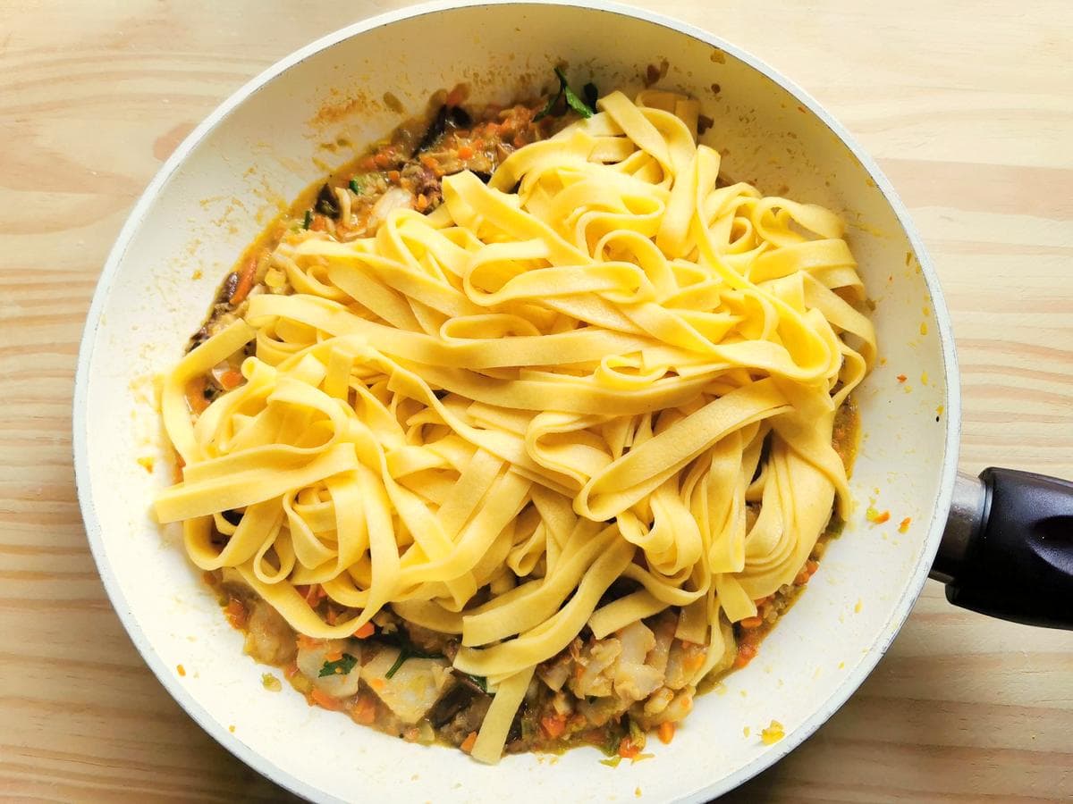 Cooked and drained tagliatelle in frying pan with baccalà and porcini sauce.