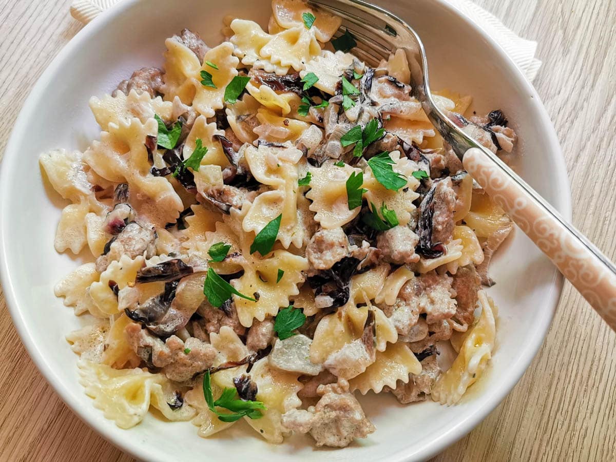 A serving of sausage and radicchio farfalle in a white bowl.