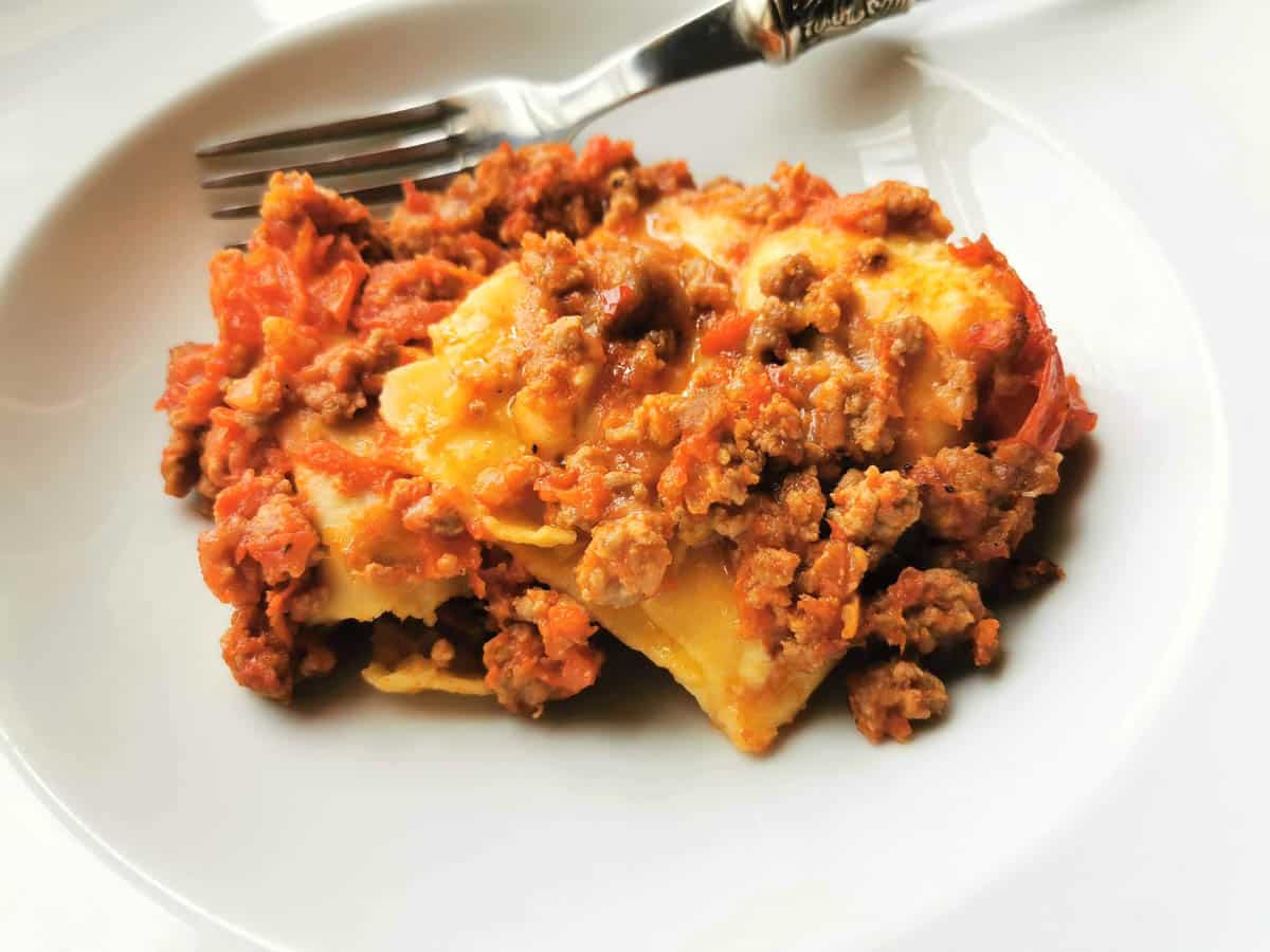 A serving of baked fazzoletti pasta with sausage ragu in a white bowl with a fork.