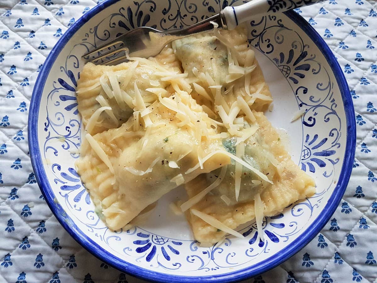 4 large ofelle alla Triestina ravioli in a blue and white bowl.