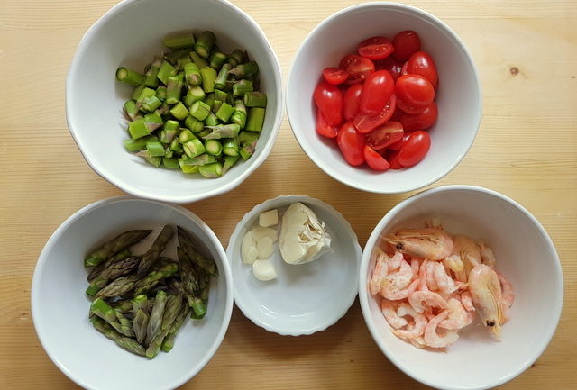 ingredients prepared for cooking chopped asparagus, separate asparagus tips, halved cherry tomatoes, cleaned shrimps and peeled garlic