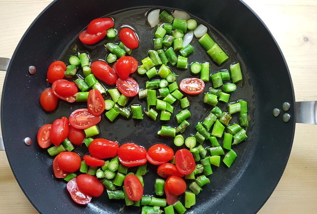 asparagus pieces, garlic and halved cherry tomatoes in frying pan