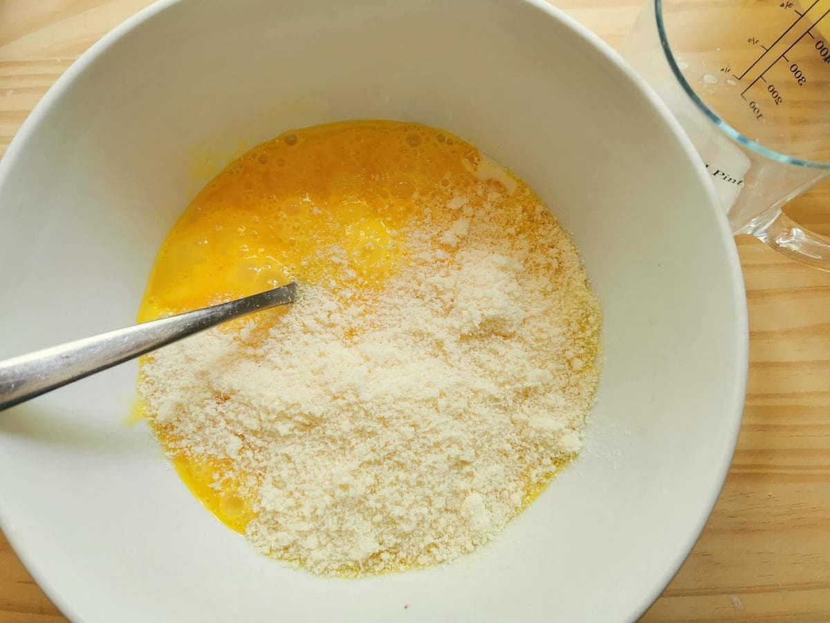 Beaten eggs with grated cheese and milk in white bowl.
