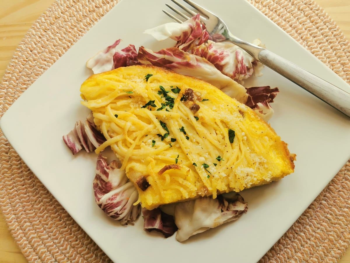 A slice of spaghetti carbonara frittata on a white plate with radicchio salad.