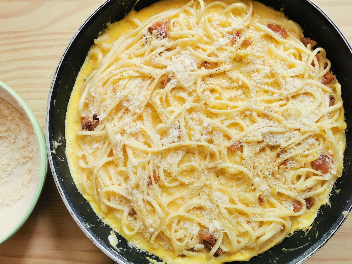 Grated Parmigiano sprinkled on half cooked spaghetti frittata.