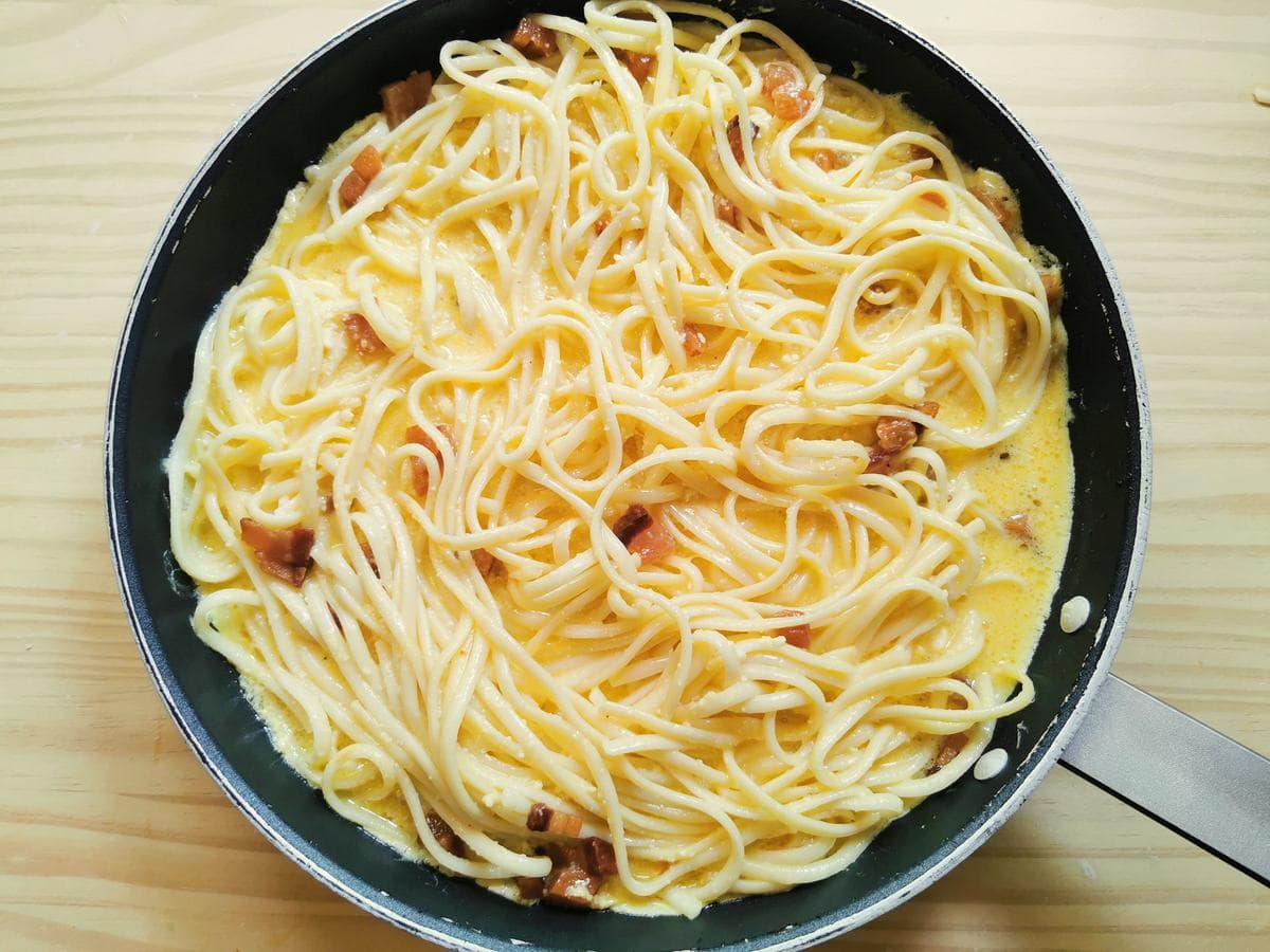 Uncooked spaghetti carbonara frittata in iron skillet.