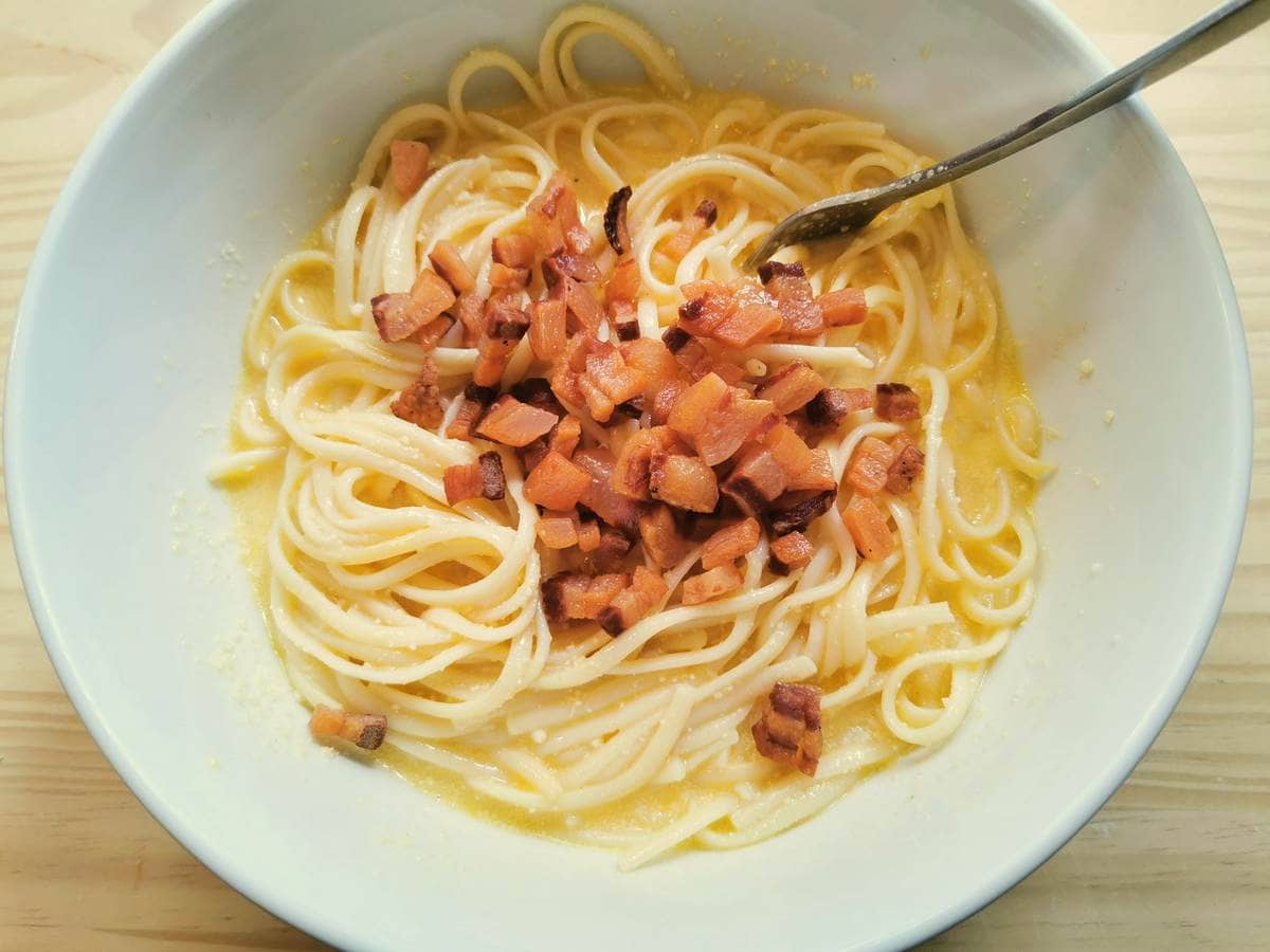 Cooked guanciale in white bowl with spaghetti and frittata egg mixture.
