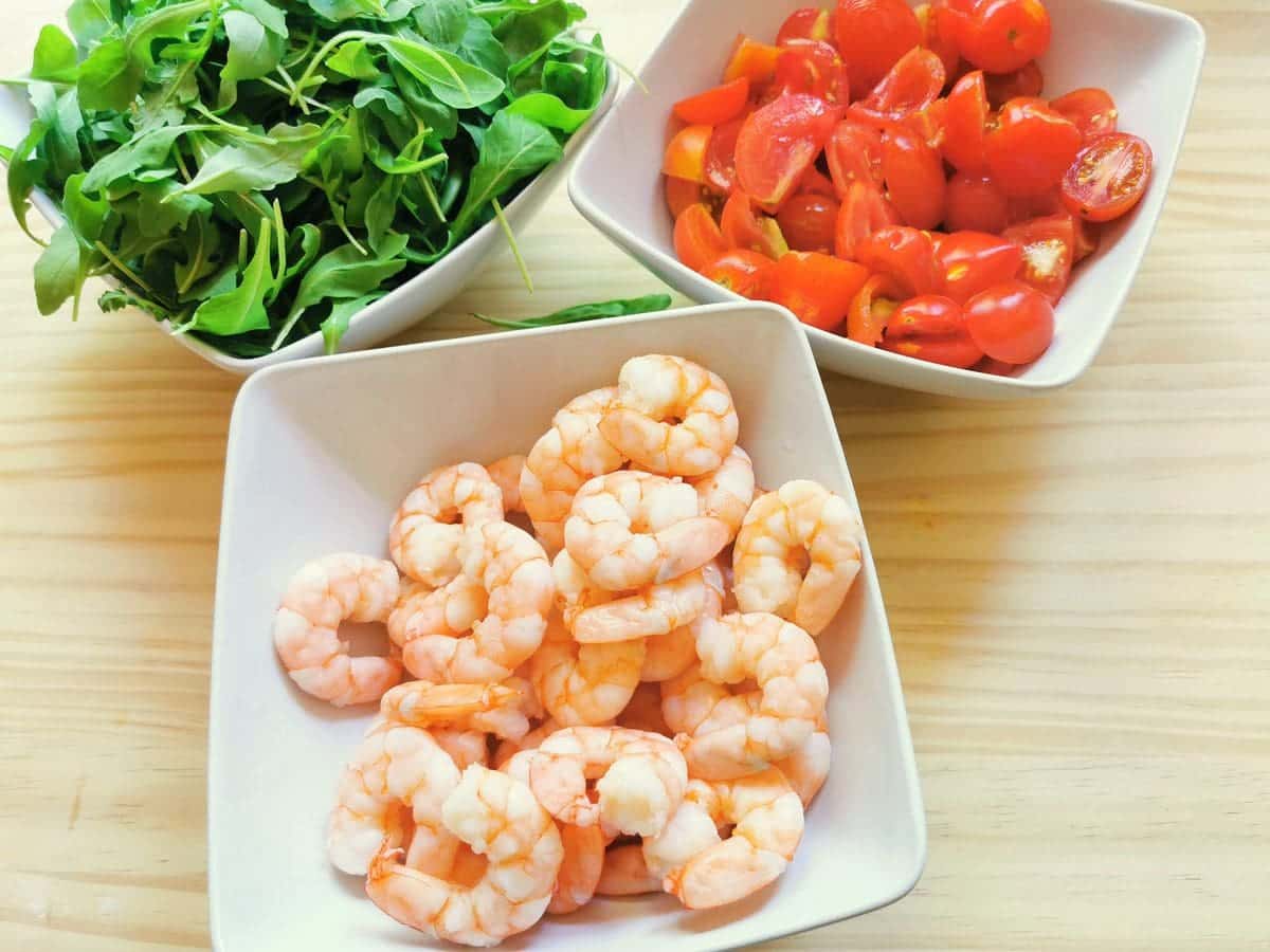 blanched prawns in white bowl, cut tomatoes in white bowl and washed rocket (arugula in white bowl