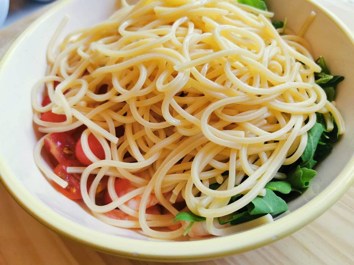 cooked spaghetti in salad bowl on top of other salad ingredients