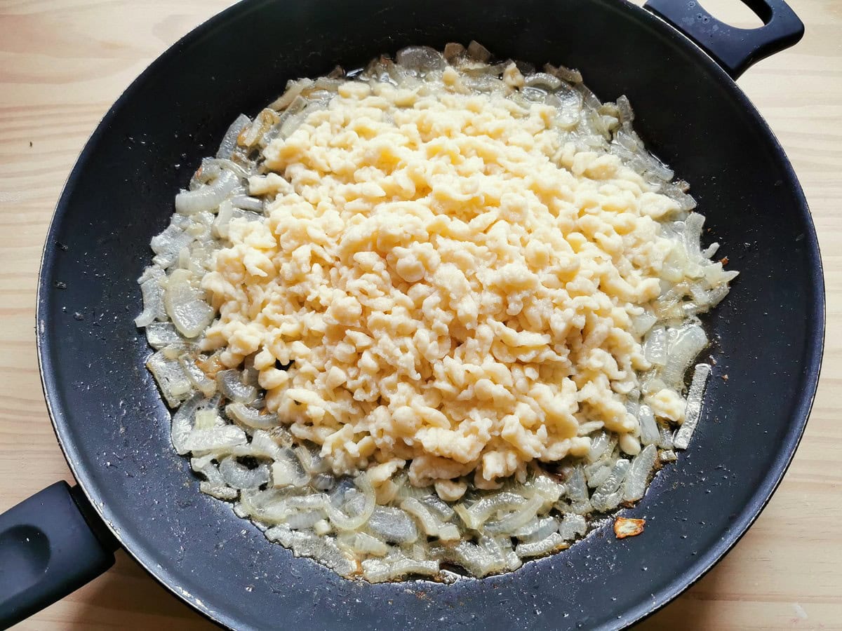 Ready cooked Italian teardrop dumplings (chnèfflènè) in frying pan with cooked onions.