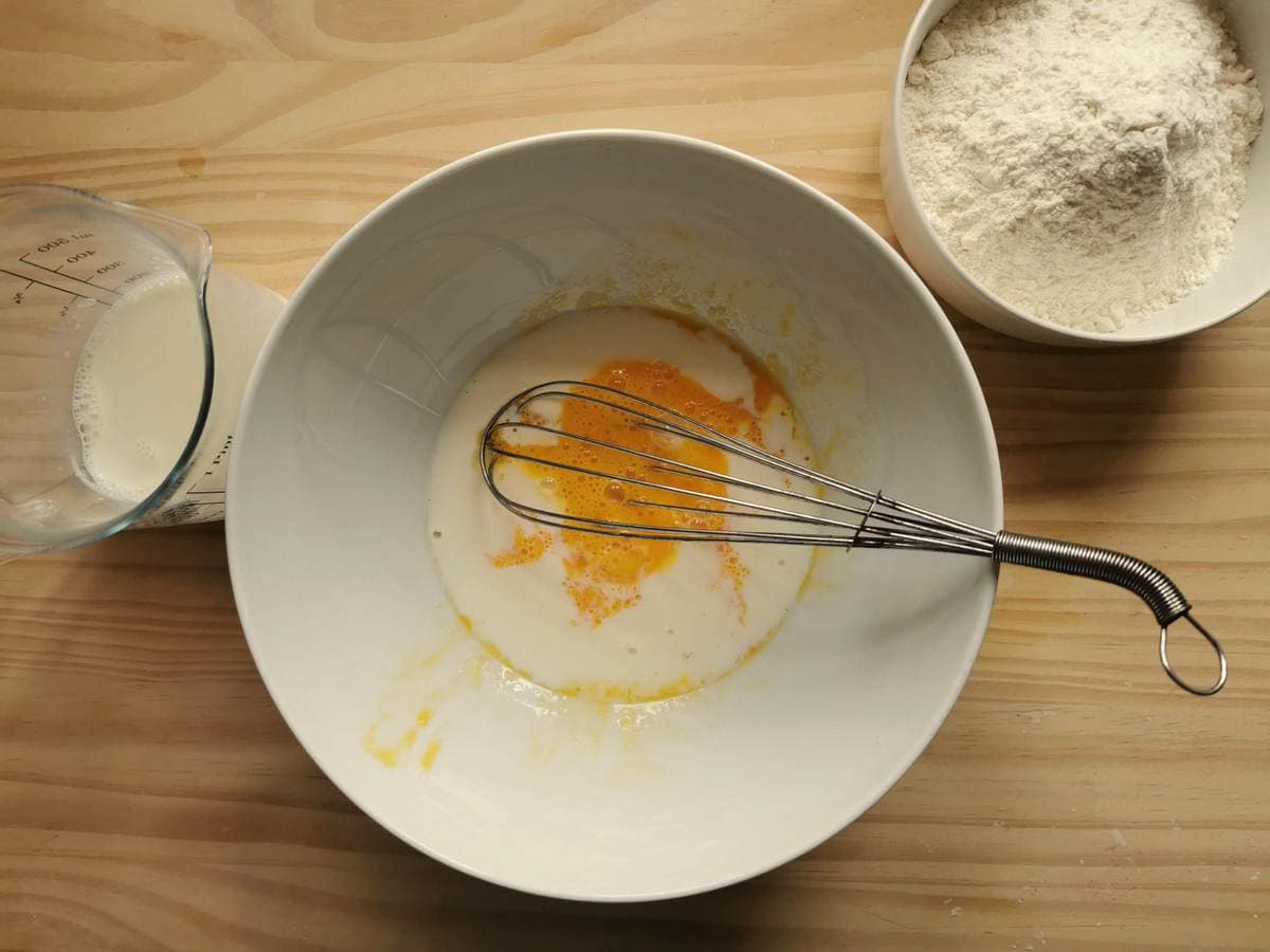 Beaten egg with milk in white bowl.