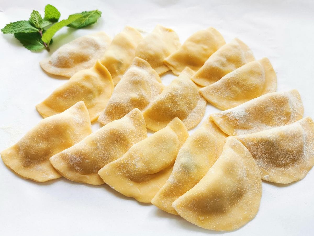 ready Ligurian potato and mint ravioli on white surface dusted with flour.