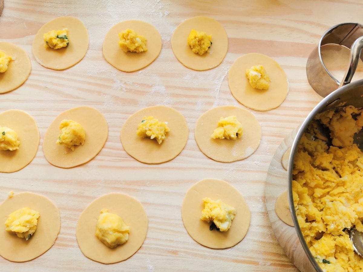 Pasta discs with teaspoon of filling in the centre on wooden pastry board.