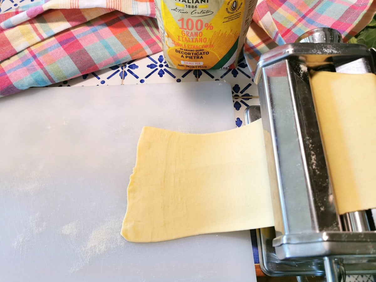 A sheet of pasta dough passing through a hand operated pasta machine.