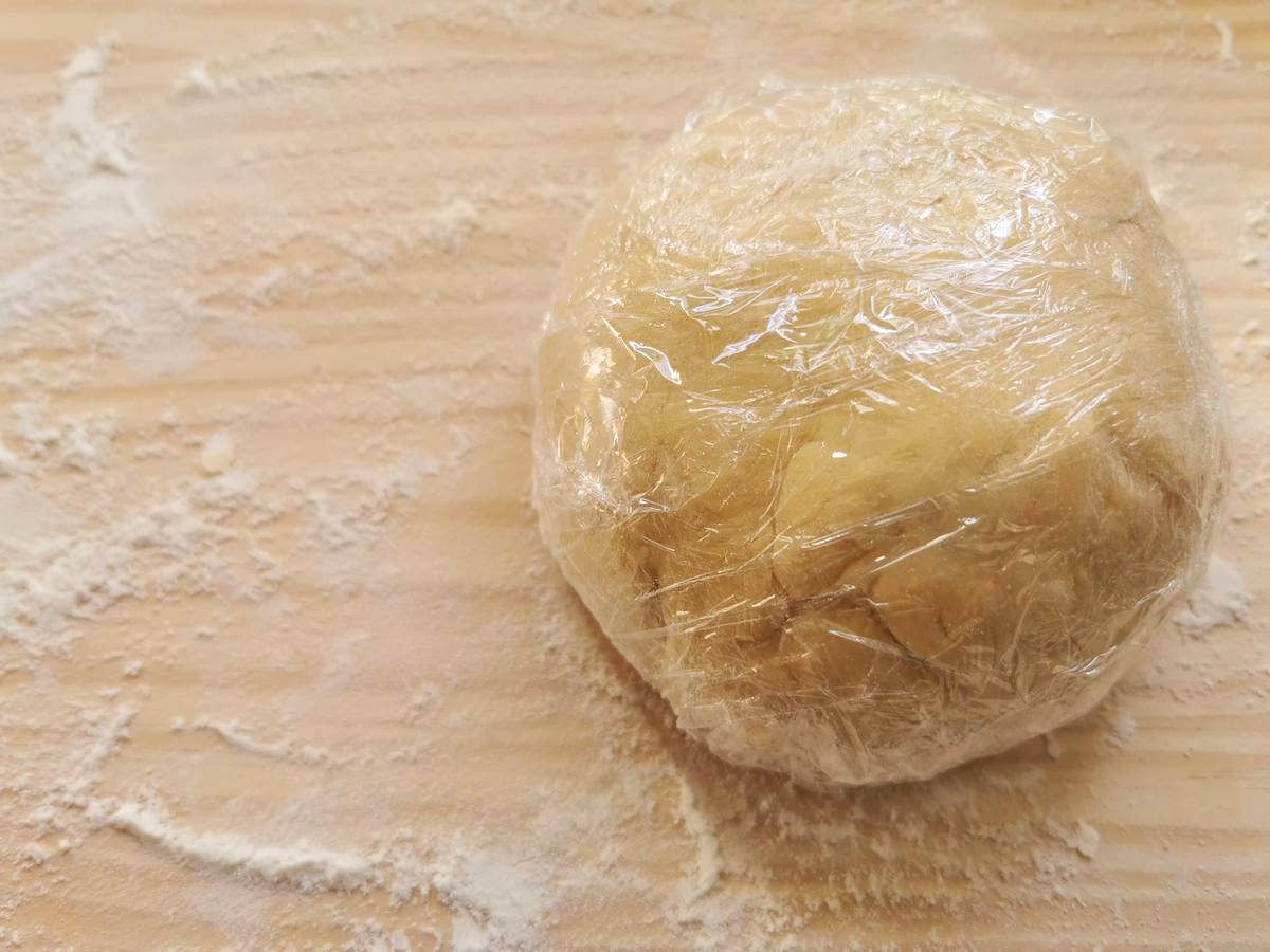 ready ball of dough wrapped in plastic wrap on wooden pastry board