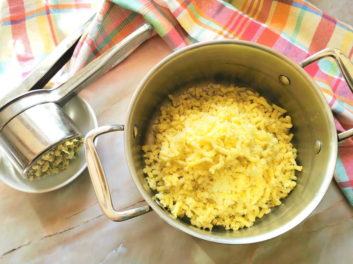 riced potato in pot and potato ricer on plate