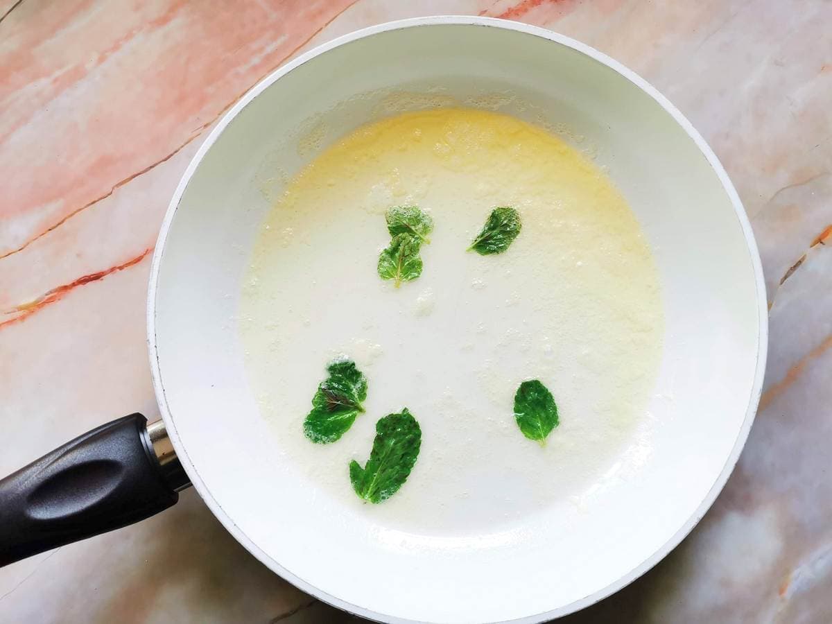 Melted butter and mint leaves in a white frying pan