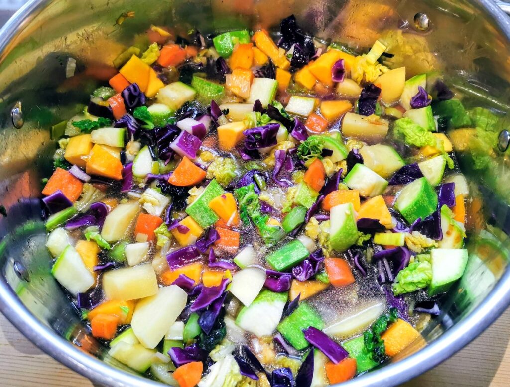 Minestrone vegetables cooking in water in large soup pot.