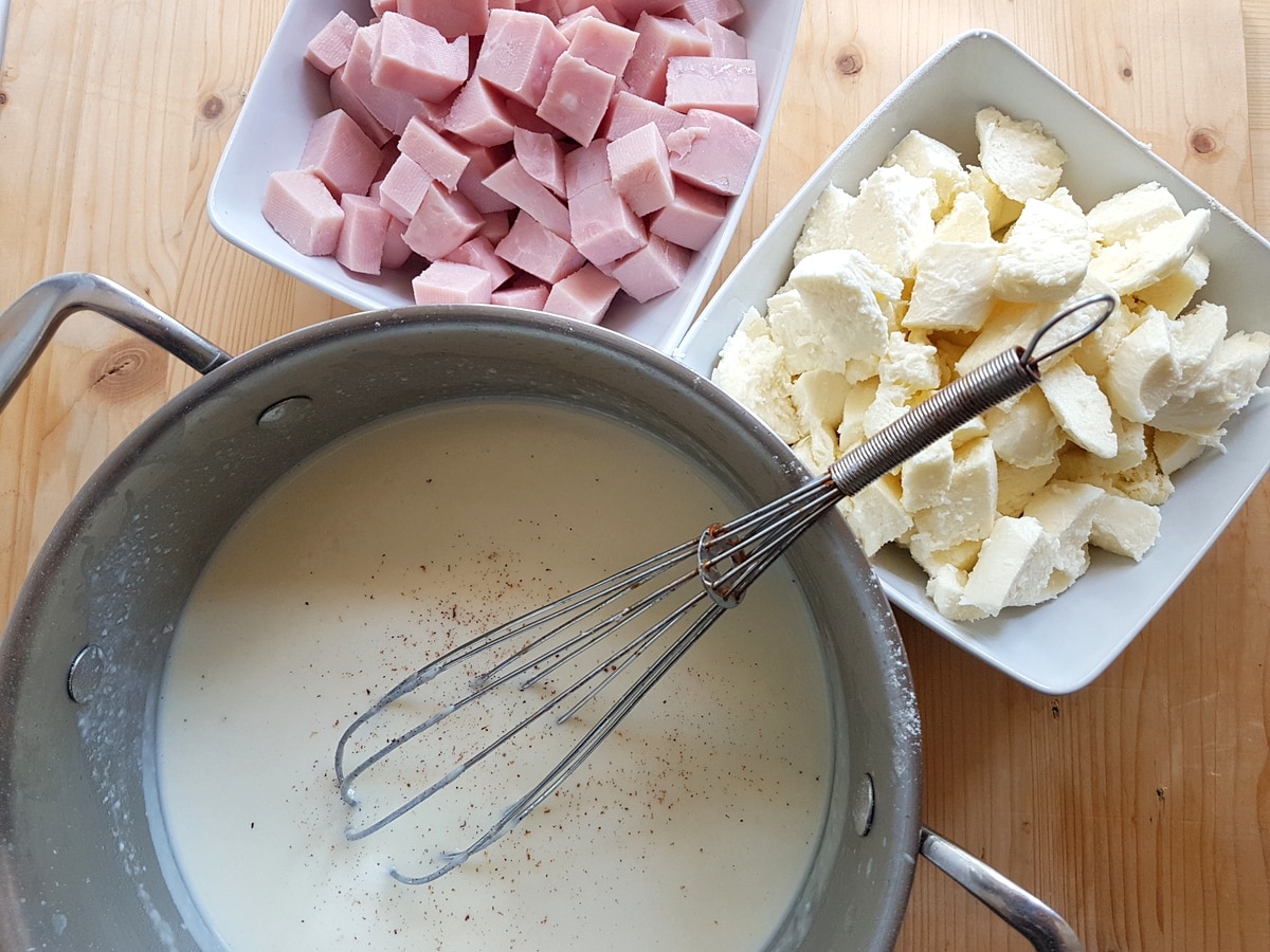 homemade béchamel in saucepan and cut ham and mozzarella in bowls