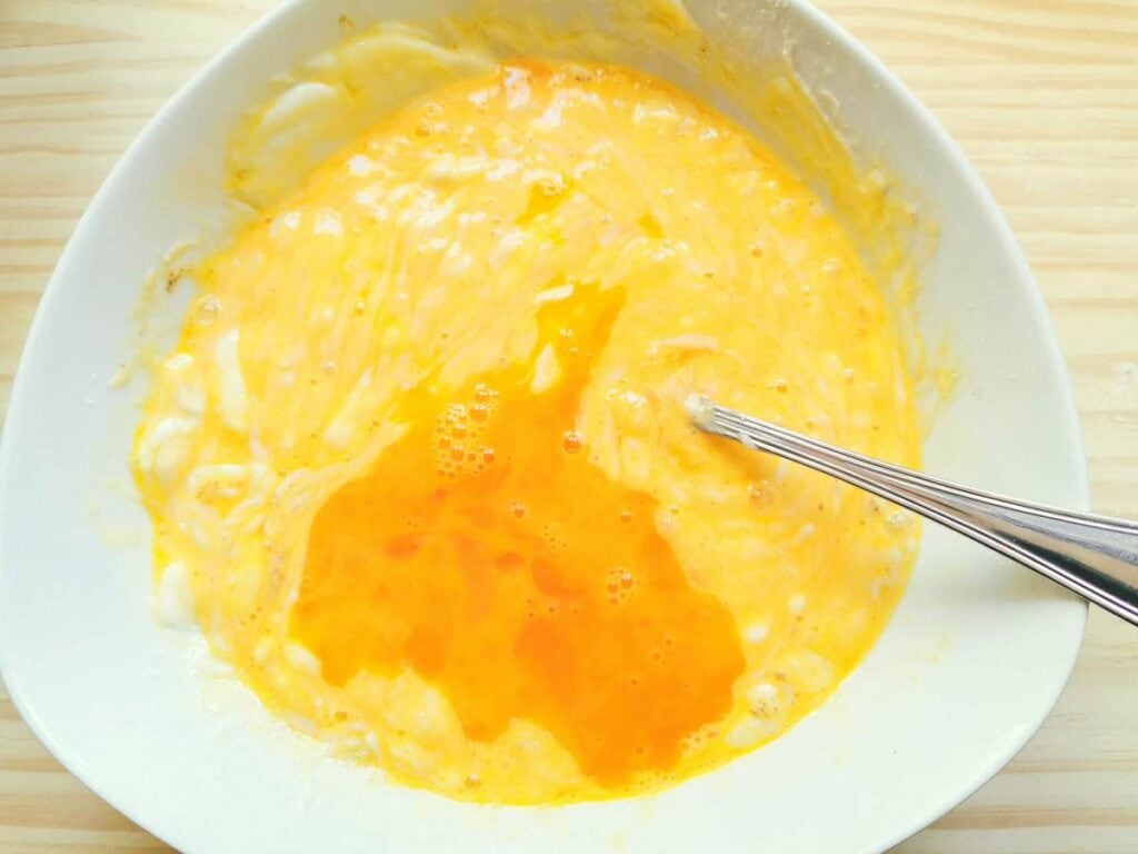 Eggs added to the ricotta mixture in white bowl