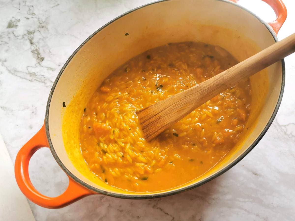 Risoni/orzo pasta cooking in pumpkin sauce in Dutch oven.