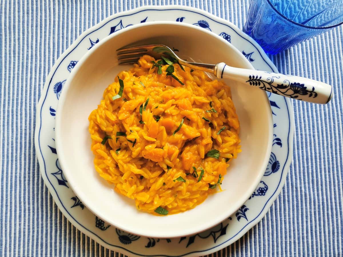 Orzo cooked risotto-style with pumpkin in white bowl on blue and white table mat.