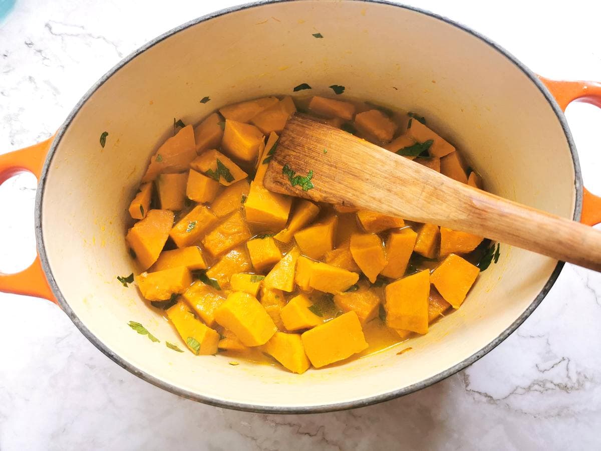 Hot vegetable stock added to the Dutch oven with pumpkin and parsley.