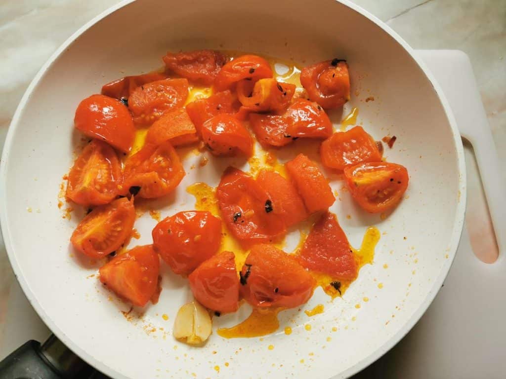 cut tomatoes cooking in frying pan with olive oil and garlic