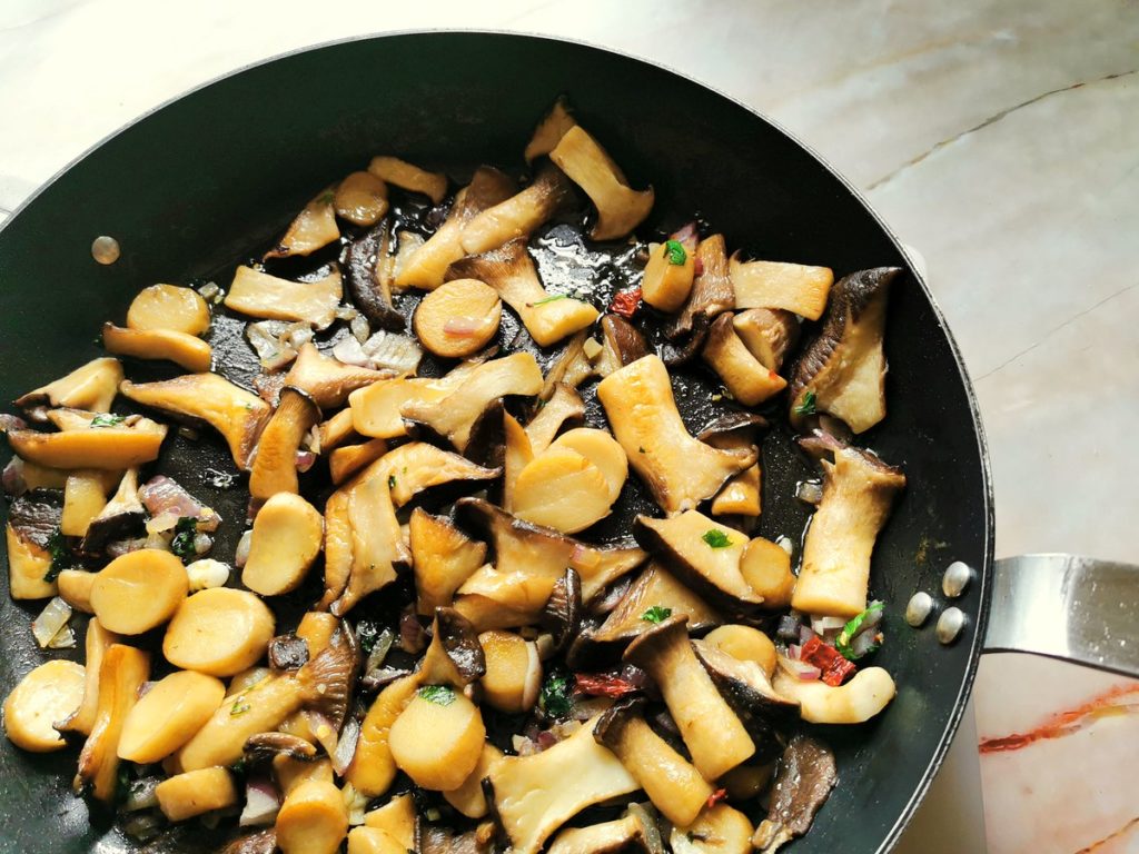 Cooked mushrooms in skillet with onions, garlic, peperoncino and parsley.