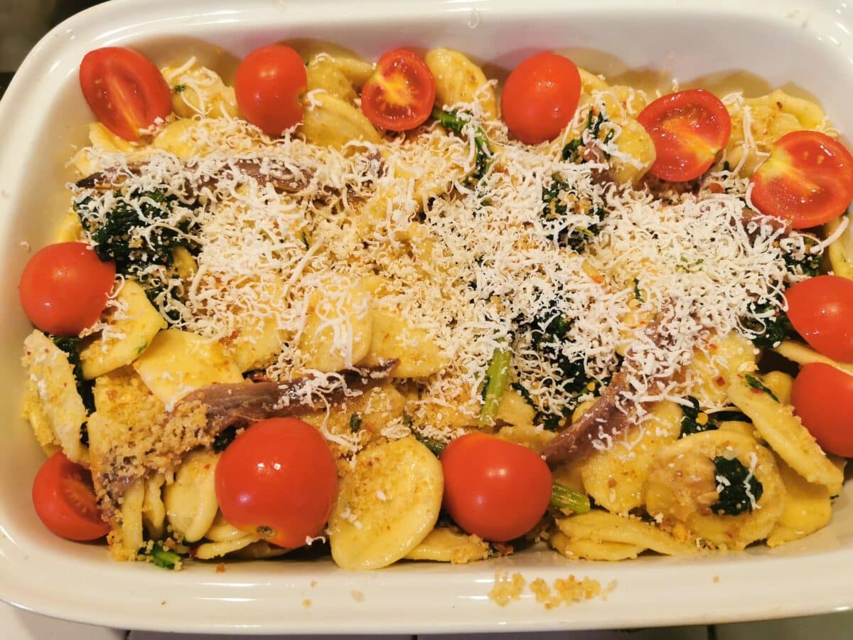 Leftover orecchiette and broccoli rabe in a baking dish with cherry tomatoes, grated cheese and anchovies. 