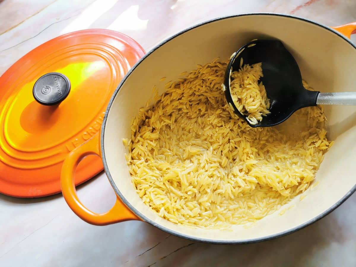 Orzo pasta in Dutch oven with some vegetable broth and a ladle.