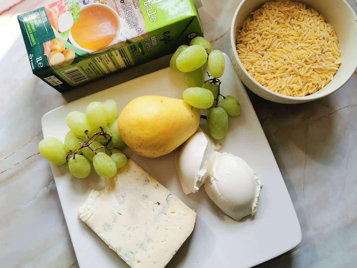Ingredients for orzo risotto with Gorgonzola. Orzo pasta, vegetable broth, Gorgonzola, mascarpone, grapes and a fresh pear on marble worktop.