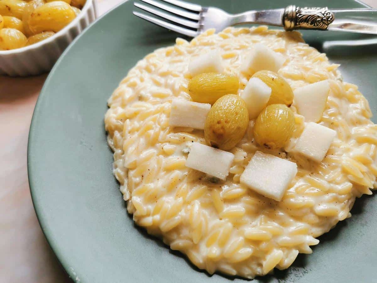 Orzo risotto with gorgonzola topped with pieces of fresh pear and roasted grapes in blue plate.