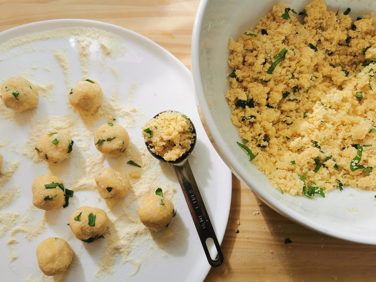 Pallotte dough in large white bowl next to plate with ready cheese and egg balls.