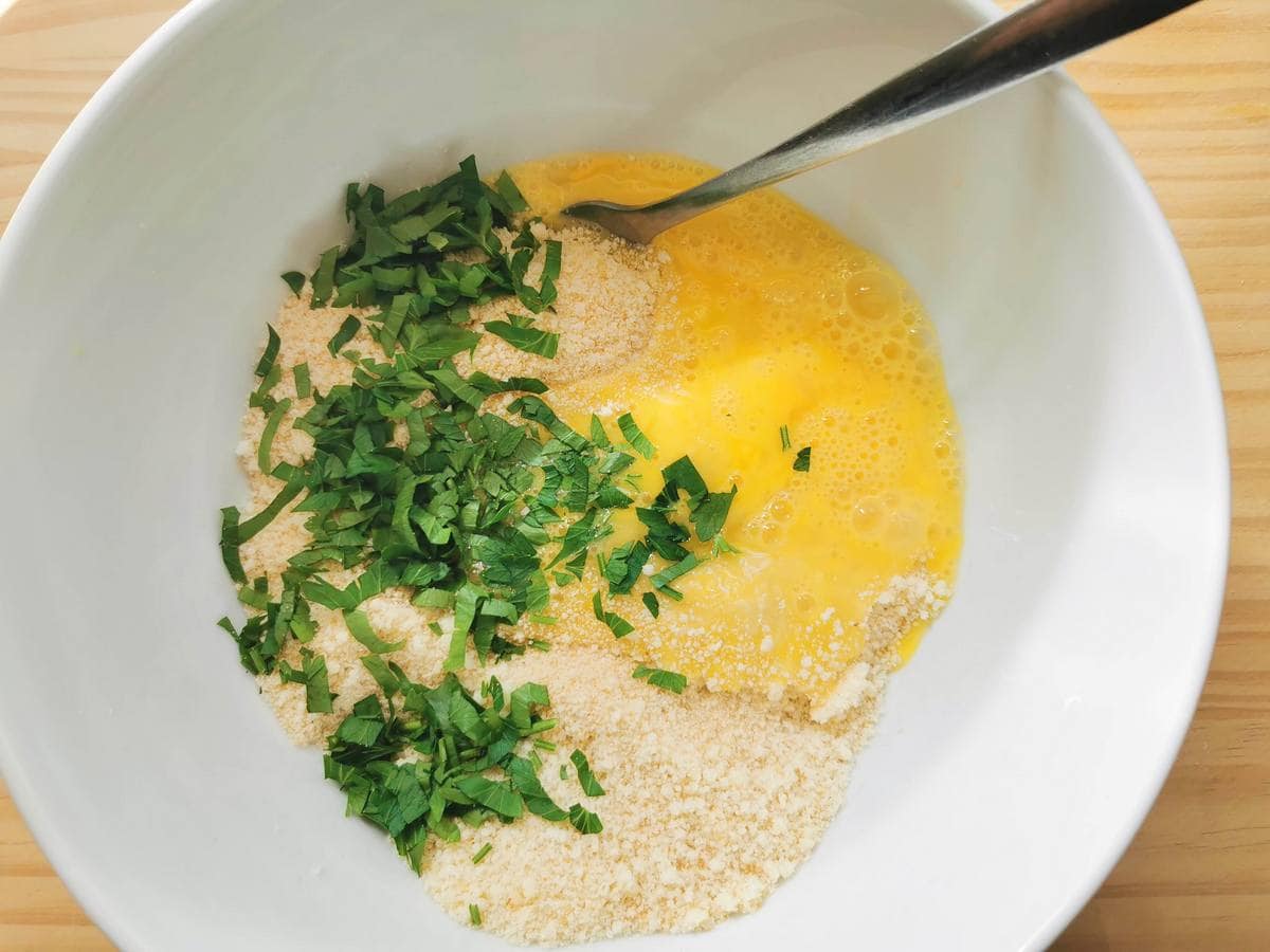 Breadcrumbs, grated cheese, eggs and chopped parsley in large white bowl