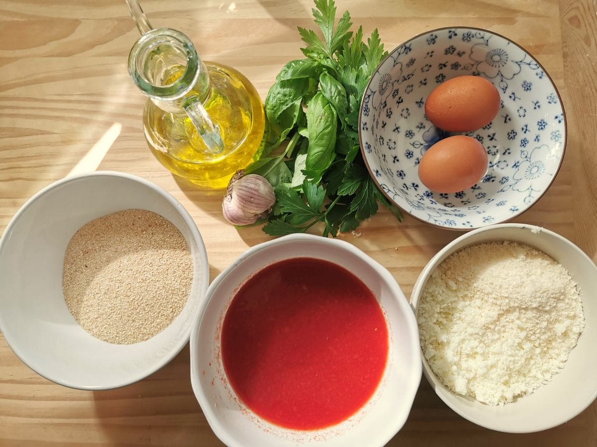 Ingredients for pallotte cacio e ova in tomato sauce; eggs, grated cheese, breadcrumbs, fresh parsley and basil, garlic, tomato passata and olive oil.