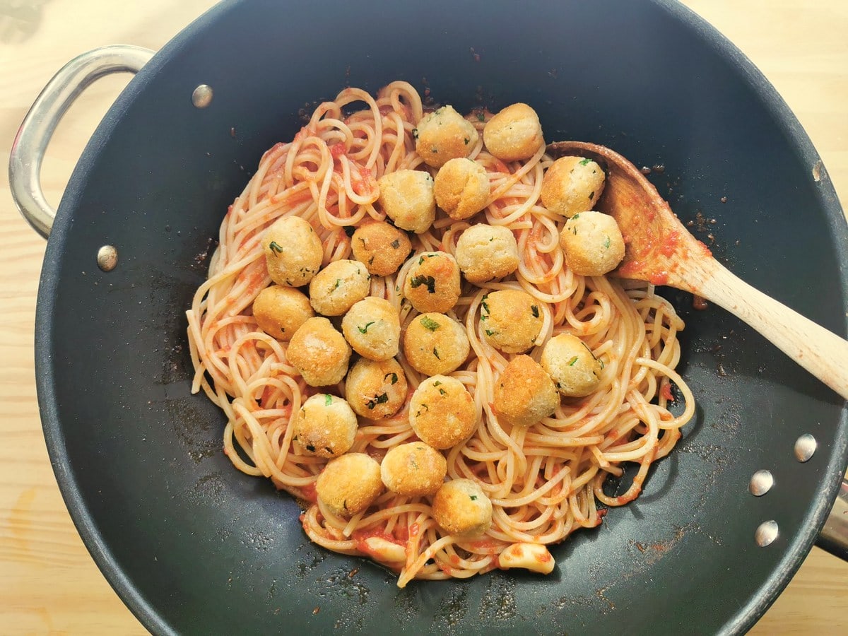 Pallotte cacio e ova added to spaghetti with tomato sauce in deep skillet.