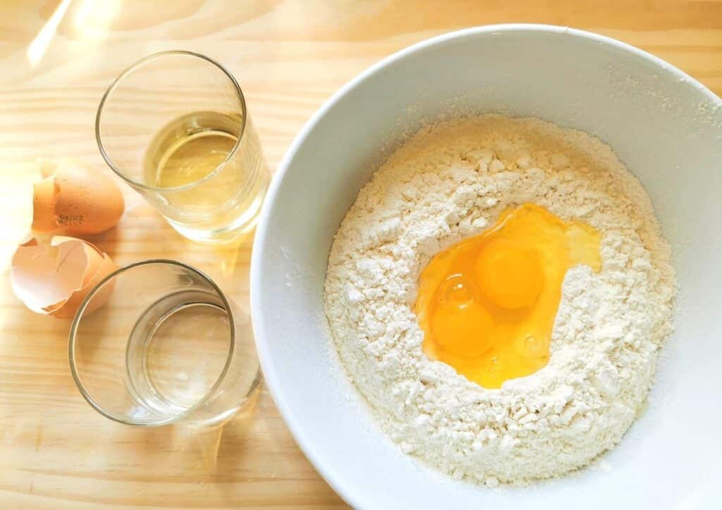 Flour and eggs in white bowl with glass of water and glass of wine.