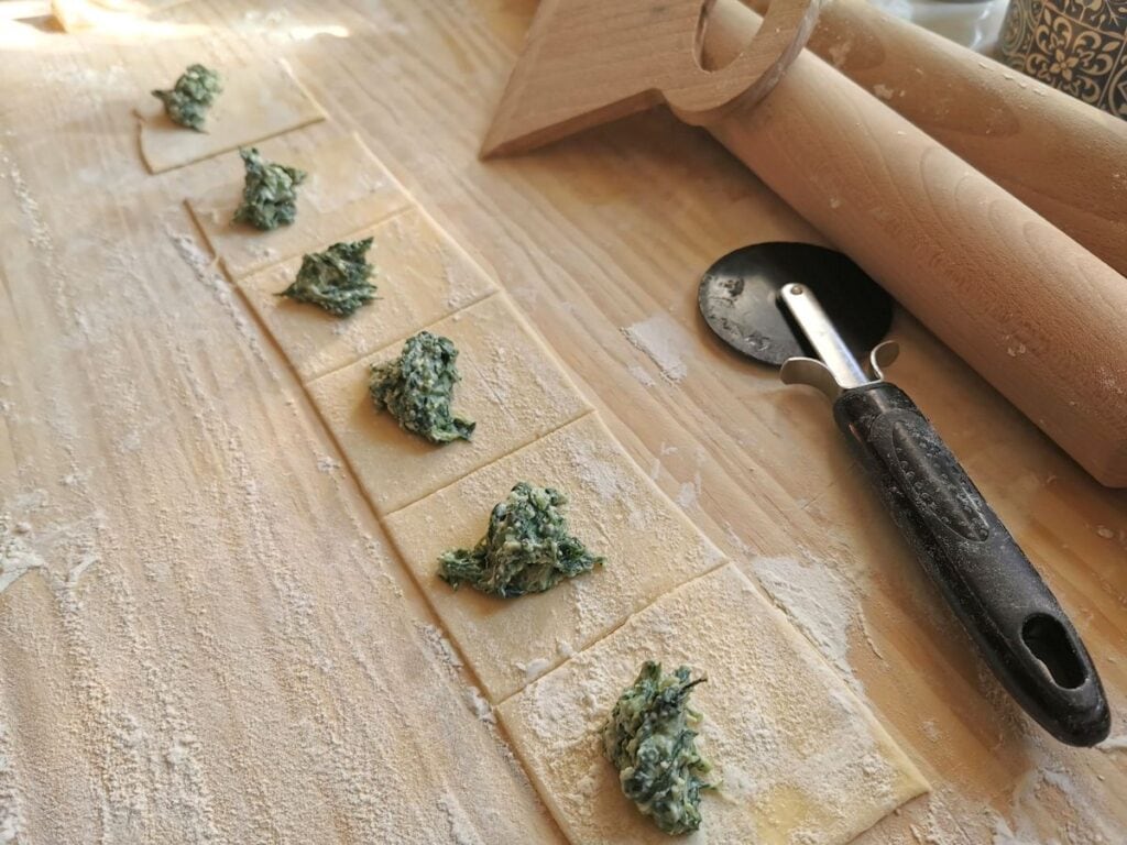 pasta dough cut into squares with a teaspoon of pansotti filling in the middle of each square.