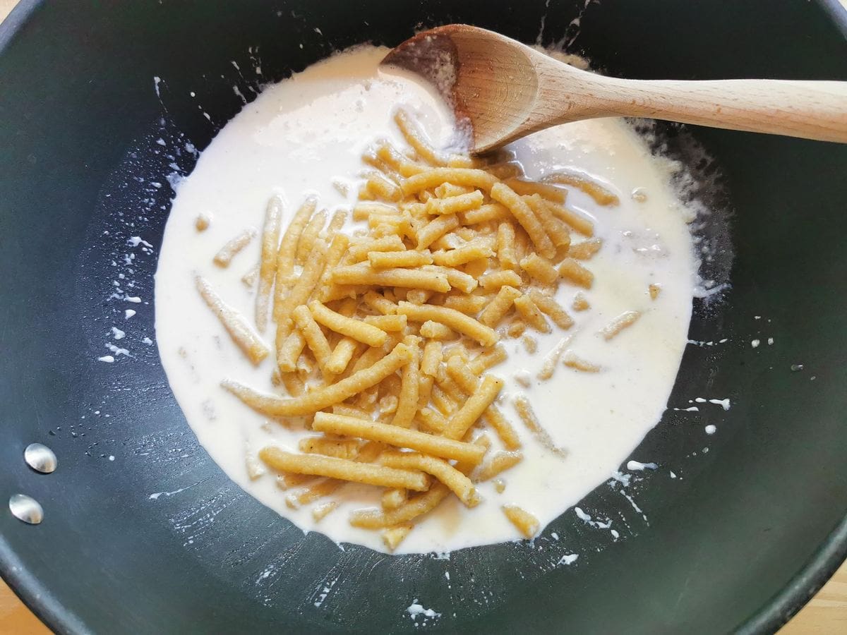 Cooked passatelli added to Parmigiano cream sauce in deep skillet.