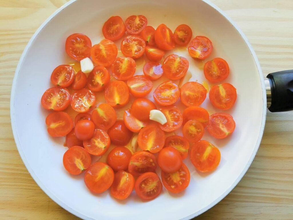 halved cherry tomatoes in pan with peeled garlic cloves and olive oil