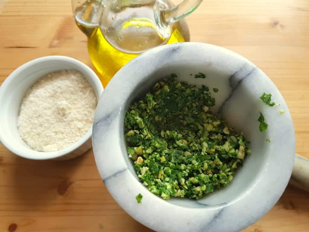 pesto in mortar with olive oil in glass bottle and pamigiano in white bowl