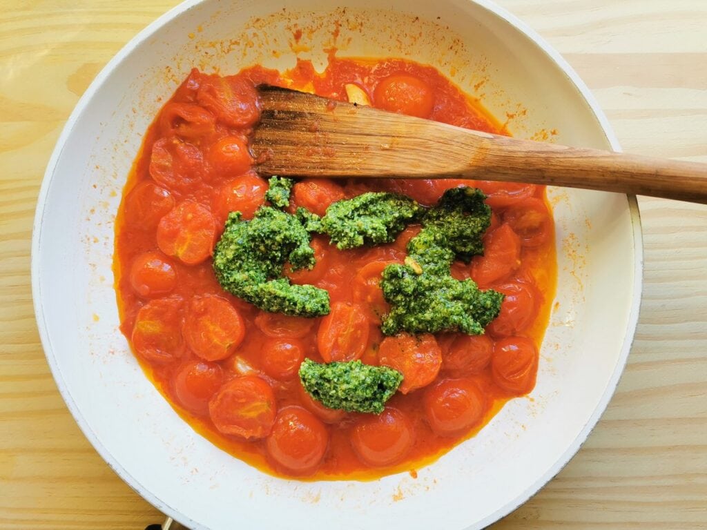 Basil pesto added to tomato sauce in pan